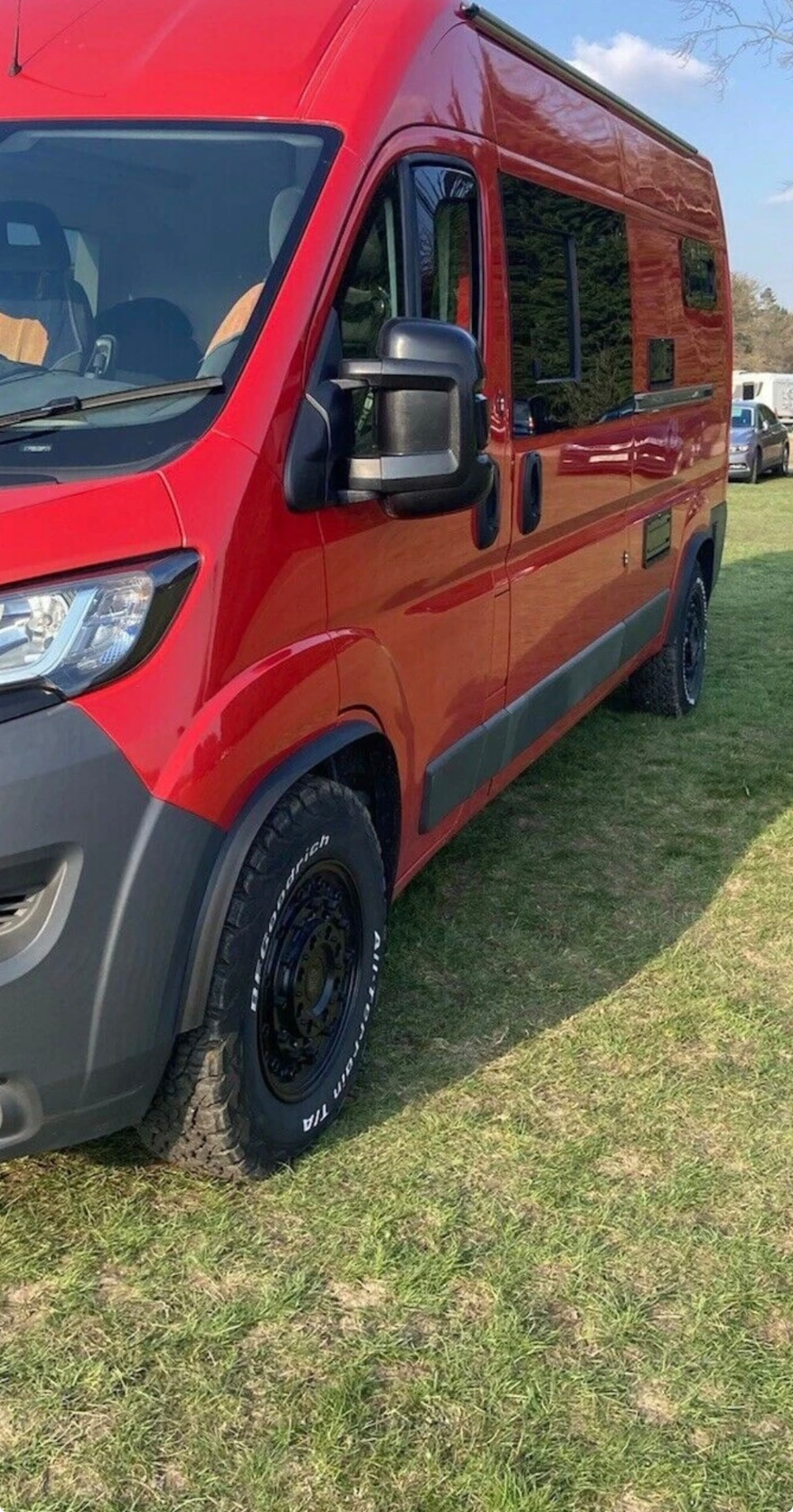 Red Peugeot Boxer camper on all-terrain tyres with extended arches and side trims