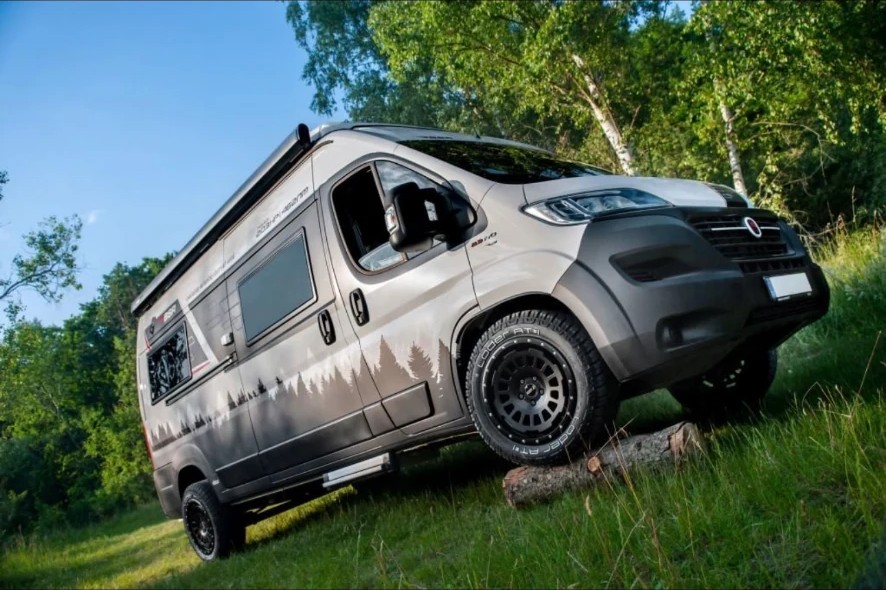 Lifted Fiat Ducato camper conversion on black alloys and all-terrain tyres parked on a grass bank