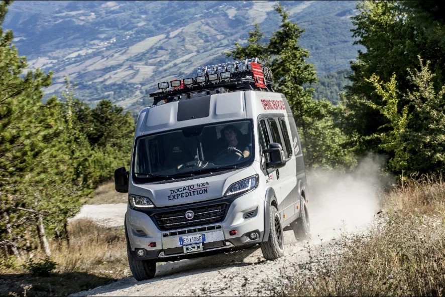 Fiat Ducato 4x4 expedition van with roof rack and LED light pods on a mountain gravel track